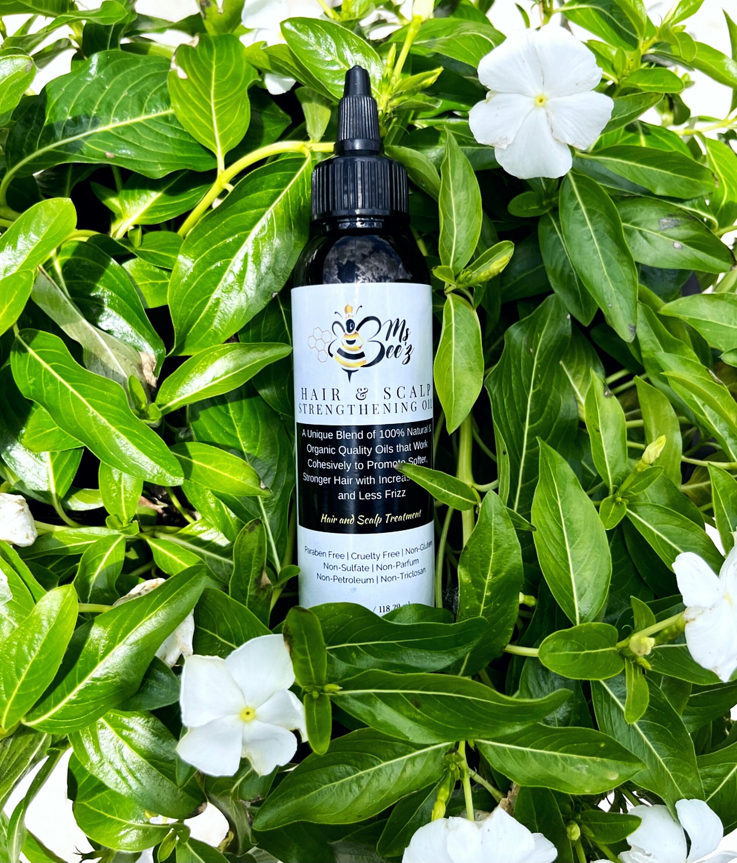 ms bee'z beauty hair and scalp strengthening oil laying in a bush of flowers